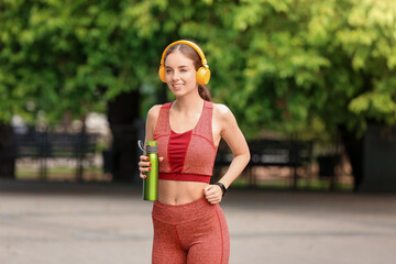 Sporty young woman with headphones and water outdoors