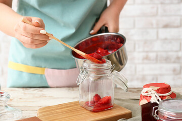Woman making sweet strawberry jam in kitchen