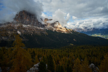 Beautiful pine tree forests with autumn colors surrounded by rocky alpine mountain ranges with cloudy sky above in The Dolomites. These iconic landscapes are located at Cinque Torri in Tyrol Italy.