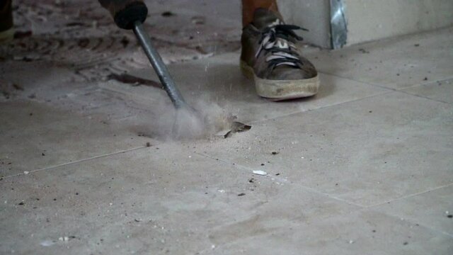 Construction worker breaking up ceramic tiles with a jackhammer in slow motion. Close up