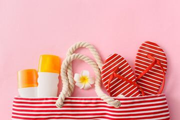 Beach bag with sunscreen cream and flip-flops on color background