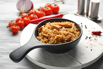 Frying pan with tasty pilaf on table