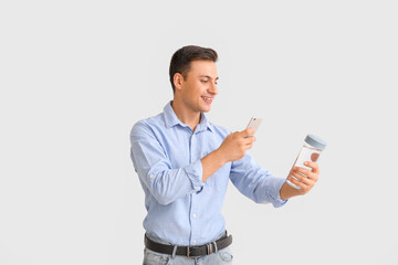 Young man with bottle of water and phone on light background