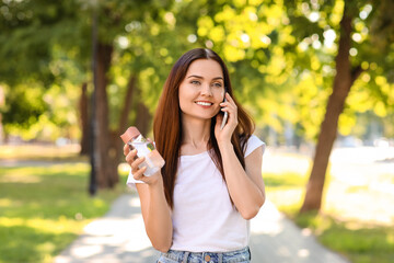 Young woman with bottle of water talking by phone in park