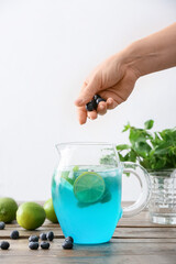 Woman making tasty blue mojito cocktail at table
