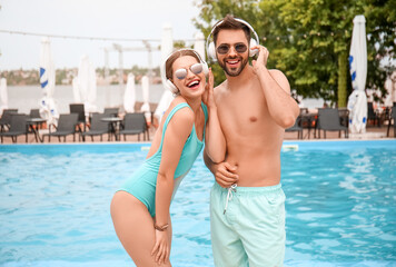 Obraz premium Young couple listening to music near swimming pool