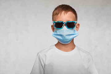 Serious boy with sunglasses weared in surgical mask and white t-shirt on a white background.   Covid-19, flu, or pollution protection and struggle concept.