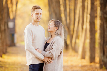Loving couple stands embracing in autumn forest in light beige sweaters, yellow background with leaves