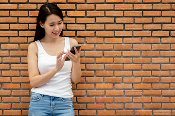 Smiling young woman using a smartphone against brick wall	
