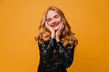 Relaxed girl in black dress posing with smile. Studio shot of carefree blonde lady isolated on...