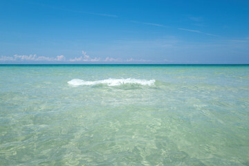Soft blue ocean wave on clean sandy beach. Tropical paradise beach with white sand. Beautiful beach with palm trees and moody sky.