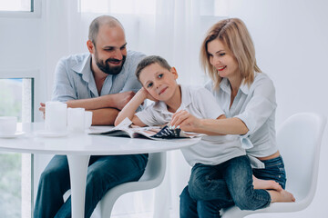 Obraz premium a cheerful family sit at a table and read a magazine. son pondered and looked side 