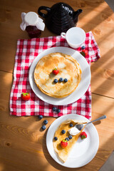 Homemade pancakes with sour cream and fresh berries on white plate on wooden table
