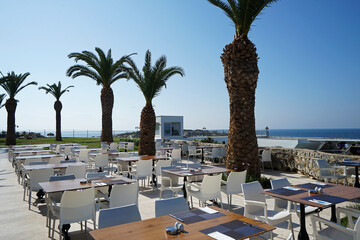 Exterior restaurant architecture and hotel dining area decoration decorated with white wooden furniture and palm tree with natural landscape view of ocean sea and clear blue sky