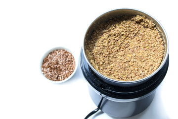 Ground flax seeds in a coffee grinder. Flax seeds in a saucer. Standing on a white background.