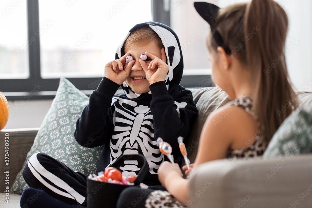 Wall mural halloween, holiday and childhood concept - smiling little boy and girl in party costumes with candie