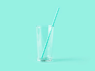 Empty tall transparent glass and paper drinking straw on mint green color background. Modern stylish tableware. Copy space.