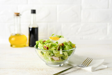 Fresh homemade salad of lettuce, cucumber, radish and boiled eggs in a glass bowl on a white wood table. Olive oil and soy sauce for dressing in the background. Healthy eating. High key shot.