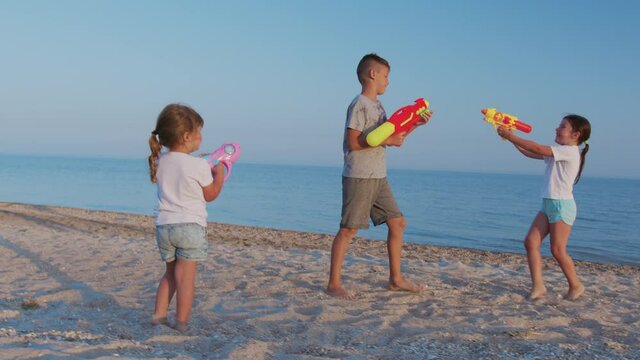 Little girls and boy on the sea. Children playing with water guns.