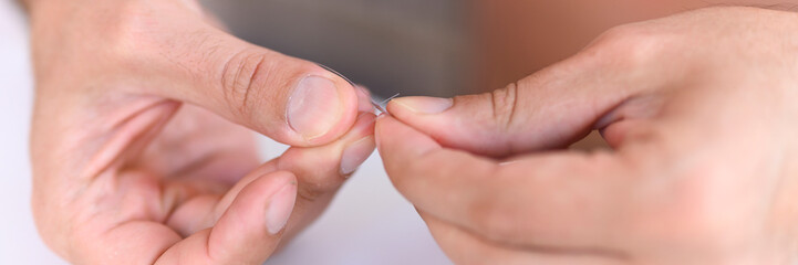 men's hands tying a fishing line with a fly on a fishing hook. selective focus. step 1. banner