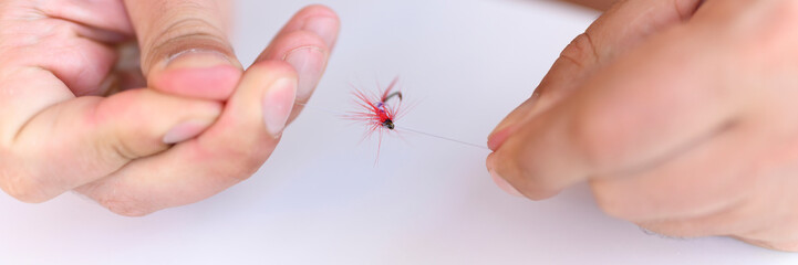 men's hands tying a fishing line with a fly on a fishing hook. selective focus. step 3. banner