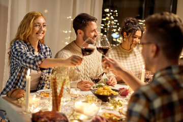 holidays, celebration and people concept - happy friends having christmas dinner party and drinking red wine at home