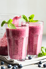 Two glasses of blueberry smoothie with mint garnish on the table. Close up view on healthy drink.