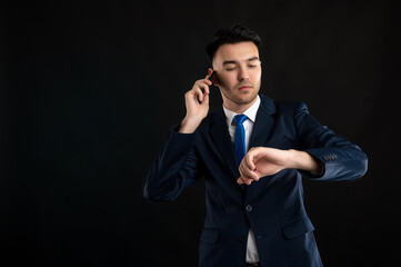 Portrait of angry business man wearing blue business suit and tie talking on the phone, looking his watch