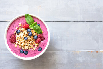 Smoothie bowl with granola and berries decorated with mint on grey wooden table. Top view with copy space.