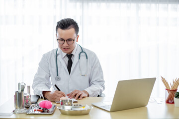 asian doctor man in uniform wear eyegrass work writing on paperwork office desk in hospital.