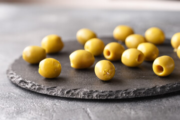Green olives on the slate plate, on the gray background.