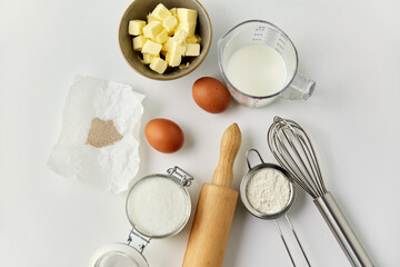 cooking food and culinary concept - rolling pin, butter, eggs, flour and cane sugar on table