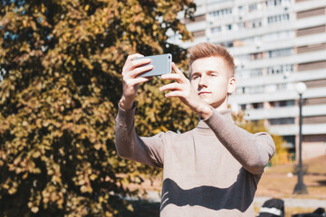 The young man holds the phone and takes pictures against the background of a multi-storey building.
