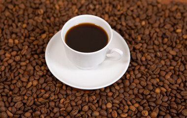 A white Cup of fragrant and hot coffee stands on the beans