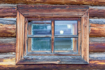 A fragment of an old wooden hut with a window. An old small window with cracks in an old wooden shack