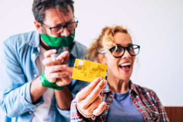 Credit card and shopping economy business concept with funny and nice adult caucasian couple with credit card - wife happy and man angry in background - focus on card