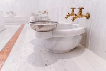 Traditional Turkish bath hammam or hamam with marble benches and sinks, taps for hot and cold water and metal bowls