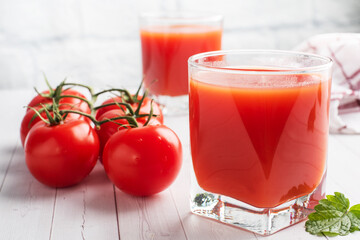 Tomato juice in glass glasses and fresh ripe tomatoes on a branch. White wooden background with copy space.