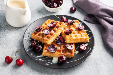 Belgian fluted waffles with fresh cherries and cream on a plate. Soft homemade waffles, sweet dessert with cherries.