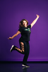 Plus size model in sportswear jumping in studio, fat woman on purple background