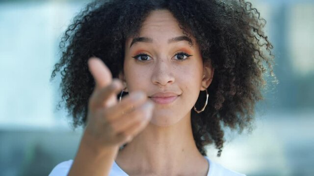 Hey you, come here, join. Beautiful African-American girl, points her index finger at camera, beckons with inviting hand gesture. Young happy woman smiles conspiratorially, intriguingly and playfully.
