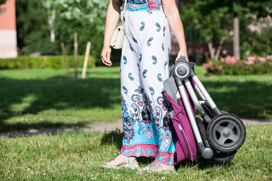 Unrecognizable Caucasian woman carrying heavy baby pushchair on green grass on lawn in summer park