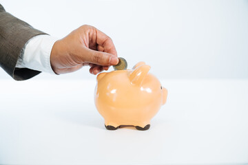 side view of a hand sticking a coin into a ceramic piggy bank on a white background