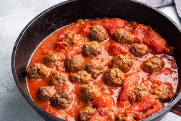 Delicious juicy Meatballs in tomato sauce are cooked in a cast iron pan. Close up Concrete background.