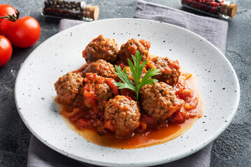 Beef meatballs stewed in tomato sauce on a plate. Dark concrete background.
