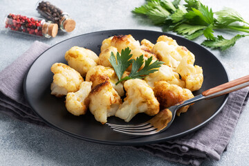 Fried cauliflower florets in batter on a black plate. Grey concrete background.