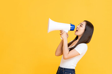 Side view portrait of young pretty Asian woman holding megaphone while shouting announcement in...