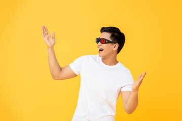 Naklejka premium Fun Portrait of excited young Asian man wearing 3D cinema glasses with both hands raised in isolated studio yellow background