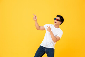 Fun Portrait of happy young Asian man wearing 3D cinema glasses pointing both fingers upward  in...
