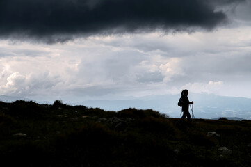 Amazing silhouette photo of woman with a nordic walking sticks, a big grey cloud above her. Hiking, backpacking
